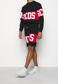 Completo felpa e pantaloni corti neri e rossi, con audace scritta bianca. La felpa ha un collo a girocoscia; i pantaloni corti hanno una vita elastica.