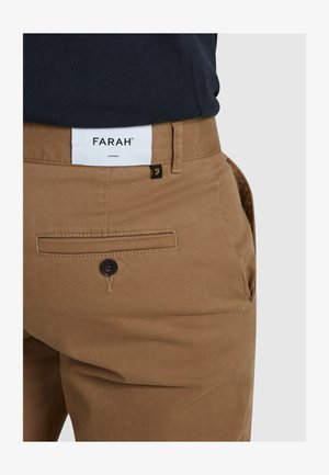 Chinos marroni realizzati in cotone con una finitura liscia, dotati di chiusura a bottone, tasche laterali e un'etichetta bianca con logo sul retro.