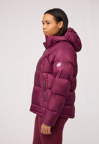 Burgundowa kurtka puchowa z kapturem, z zamkniętą kieszenią boczną i okrągłym logo na rękawie. Gładki, błyszczący materiał z pikowanymi sekcjami.