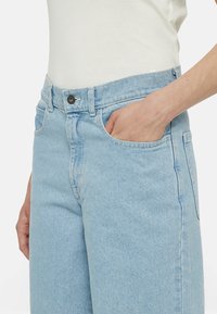 Světle modré džíny z denimu s hladkou texturou, vysokým pasem, designem s pěti kapsami a kovovým zapínáním v přední části.