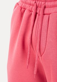 Close-up af lyserøde joggingbukser med elastisk taljebånd, matchende snore og sidelomme detalje.