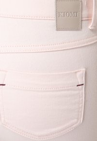 Ljust rosa denimjeans har en bakficka med kontrasterande mörkröd söm och en rektangulär märkessnutt märkt "KIOMI."