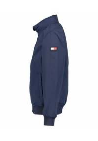 Marineblaue Bomberjacke mit hohem Kragen, gerippten Bündchen und Bund; auf dem Ärmel befindet sich ein kleines Emblem in Rot, Weiß und Blau.