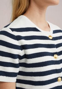Raidallinen neulecardigan tummansinisessä ja valkoisessa, johon kuuluu lyhyet hihat, pyöreä pääntie ja kultaiset nappiaksentit edessä.
