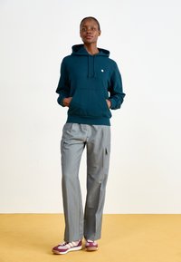 Teal hoodie with kangaroo pocket, gray cargo pants with side pockets, and maroon sneakers with white stripes and gum sole.