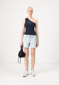 Mørkeblå one-shoulder bodysuit med stjernebroderi, kombinert med lyseblå høytlivede shorts og hvite sneakers. Svart blomsterveske inkludert.