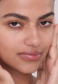 Close-up van een gezicht met een egale huid, gedefinieerde wenkbrauwen en volle lippen. De teint is gelijkmatig en natuurlijk, met een subtiele glans en een gezonde textuur.