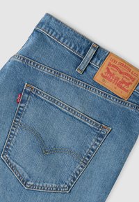 Poche arrière d'un jean Levi's bleu plié avec couture visible, étiquette rouge, passants de ceinture et patch en cuir de la marque sur la ceinture.