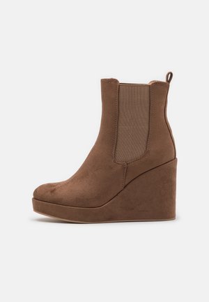 Brązowe zamszowe botki na koturnie za kostkę z elastycznymi panelami bocznymi, okrągłym czubkiem i pętlą z tyłu ułatwiającą zakładanie.