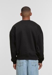 Schwarzer Sweatshirt mit überschnittenen Schultern, gerippten Bündchen und Saum. Weicher Stoff. Getragen mit hellblauen Jeans. Einfaches, einfarbiges Design.