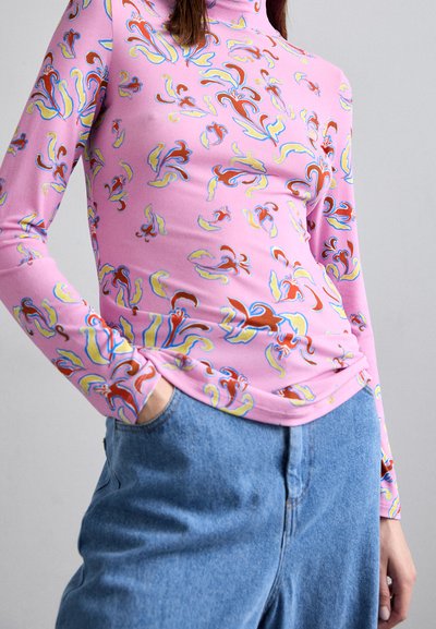 Langermige turtleneck top van roze stof, uitgerust met multikleurige abstracte patronen, gecombineerd met hoog-waisted blauwe denim jeans.