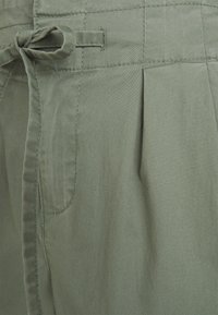 Calças de algodão verde-azeitona com cintura ajustável, apresentando pregas e bolsos laterais. O tecido possui uma textura suave e um brilho subtil.
