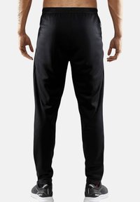 Sorte træningsbukser lavet af glat, strækbart materiale med en taperet pasform, der har sidesømme og en ribbet talje.