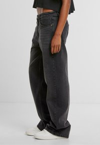 Zwarte denim wijde broek met een hoge taille, voorzien van een knoopsluiting en voorzakken. Ggedragen met witte sneakers.