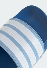 Blå halksandaler med texturerad ovandel, breda vita ränder och en slät sula. Dubbla blå nyanser framhäver dess moderna design.