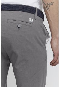 Pantalones grises de tela texturizada, con un cinturón de lana azul marino trenzado, bolsillo trasero abotonado y detalles en los bolsillos laterales.