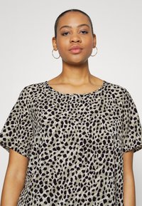 T-shirt à manches courtes avec un col rond, arborant un motif à pois noir et beige. Tissu doux avec une coupe décontractée.
