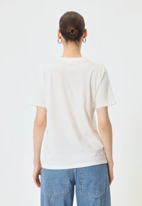Hvid kortærmet t-shirt lavet af bomuld, med en rund halsudskæring og en afslappet pasform. Bagfra viser den et simpelt design uden udsmykninger.