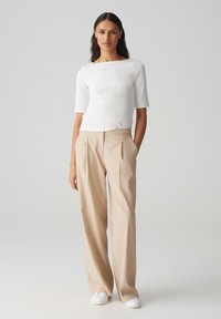 Witte geribde top met korte mouwen, gecombineerd met beige geplooide wijde broek en witte sneakers, met een eenvoudig en schoon ontwerp.