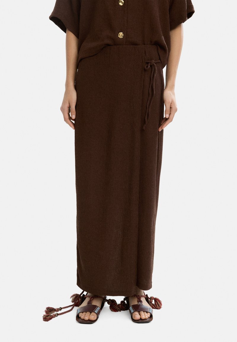 Brąskowy, teksturowany maxi spódnica z talią na sznurek. Połączona z płaskimi sandałami ozdobionymi frędzelkami i kolorowymi akcentami.