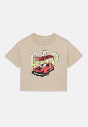 T-shirt cropped beige avec le motif "CAP" et une graphique de voiture de sport rouge, des rayures noires et une bannière "Hot Wheels" en couleurs vives.