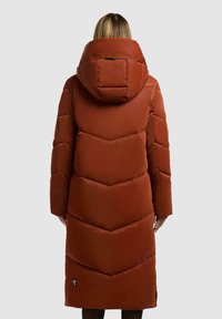 Cappotto lungo imbottito di colore ruggine con un design a quadri a zigzag, isolamento in piuma d'anatra e un grande cappuccio. Include un accento con logo nero sul lato sinistro.