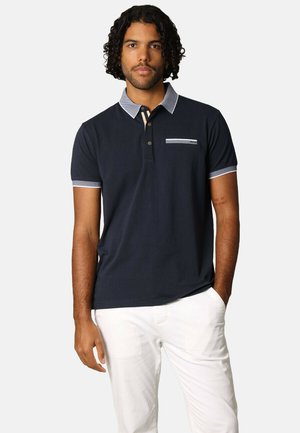 T-shirt polo navy avec un col, des bordures contrastantes bleu clair sur les manches, et une poche poitrine. Texture douce et coupe décontractée.