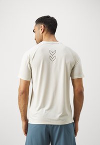 Light beige short-sleeve shirt with textured fabric. Features a round neckline and three downward chevrons in dark color on the back.