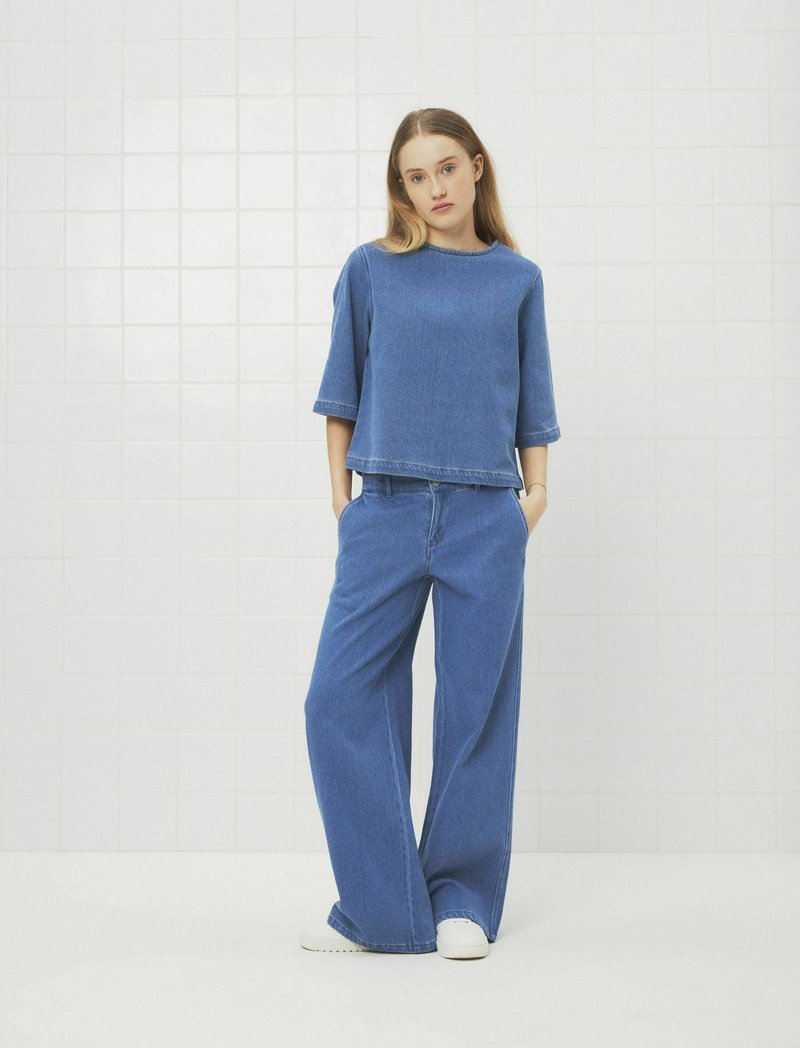 Denimtop och vida byxor i ljusblått. Toppen har en rund halsringning och en kort design; byxorna har en lös passform och fem fickor.