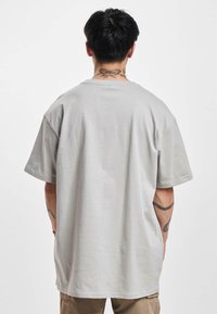 Lysegrå oversized t-shirt lavet af bomuld. Har en rund halsudskæring og korte ærmer. Glat tekstur med et enkelt design.
