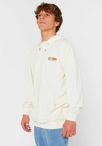 Crème-kleurige hoodie met een trekkoordcapuchon, ribbelmanchetten en een fronstzak; heeft het "RIP CURL" logo in oranje op de borst.