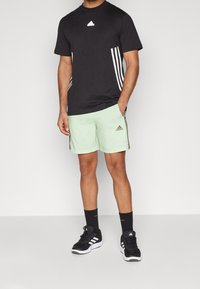 Svart idrottströja med vitt logotyp, kombinerat med ljusgröna shorts med svarta sidostripes och detaljer; svarta sportskor och strumpor.