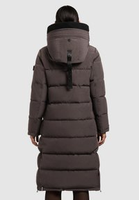 Lungo cappotto imbottito grigio con un grande cappuccio foderato in pile nero, trapuntatura orizzontale, tasche laterali con zip e una cinghia posteriore regolabile.