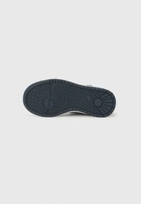 Black rubber shoe sole with a textured tread pattern, featuring rounded edges and a circular logo in the center for improved traction.