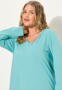 Türkisfarbenes Longsleeve-Oberteil mit V-Ausschnitt, hergestellt aus glattem, leichtem Stoff. Hat eine lockere Passform und ein einfaches Design.