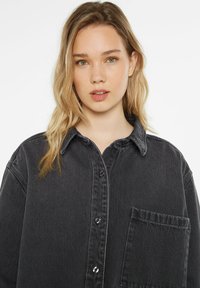 Black denim shirt with a button-up front, collar, and chest pocket; features light stitching and a relaxed fit.