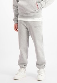 Grijze sweatshirt en bijpassende sweatpants van zachtstof; met elastische boorden en tailleband, met een logo op de broek. Witte sneakers.