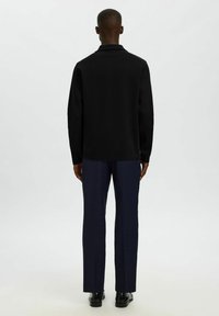 Zwarte lange mouwen trui met kraag, gecombineerd met marineblauwe rechte broek. Glad textuur en op maat gemaakte pasvorm, bekeken vanuit de achterkant.