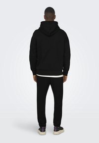 Sudadera negra con capucha, con puños y dobladillo acanalados, combinada con pantalones de chándal negros a juego. Confeccionada en una tela suave y lisa.