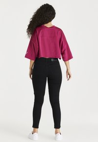 Top corto magenta con mangas anchas, combinado con vaqueros ajustados negros y zapatillas blancas. El top presenta una textura suave y un ajuste relajado.