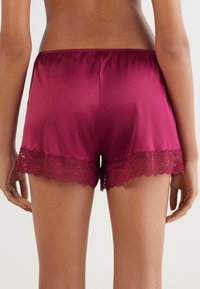 Bordeaux satijnen shorts met een delicate kantafwerking aan de zoom, voorzien van een elastische tailleband en een gladde textuur.