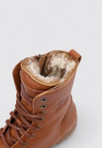 Bota de cuero marrón con un suave forro de piel, diseño de cordones y ojales metálicos. Incluye una asa en la parte trasera para facilitar su uso.