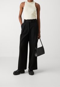 Pantaloni neri a gamba larga con vita alta e cinta, abbinati a un top aderente color crema e una piccola borsa nera. Scarpe nere spesse.