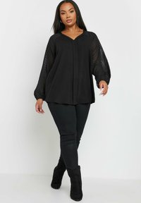 Black blouse with a V-neck and puffed, striped long sleeves; paired with black skinny jeans and black ankle boots. Smooth fabric, loose fit.