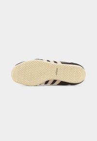 Σόλα παπουτσιού Adidas με σχέδιο πέλματος σε ζιγκ-ζαγκ σε μπεζ χρώμα, με το λογότυπο Adidas στο κέντρο, πάνω σε απλό λευκό φόντο.