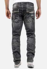 Jeans da uomo in denim grigio con finitura scolorita, dotati di tasche posteriori decorate con cuciture decorative e un'etichetta del marchio sul girovita.