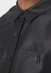 Gros plan sur le col et les poches poitrine d'une chemise noire à boutons avec des boutons noirs sur tissu foncé.