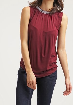 Bordeaux mouwloze top met een geplooide halslijn, voorzien van decoratieve stiksels. Gladde stof met een ontspannen pasvorm, gecombineerd met donkere jeans.