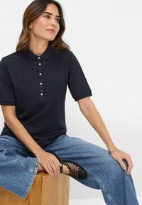 Marine polo skjorte med korte ærmer, fem knaplukning, glat tekstur. Sammen med løstsiddende blå denimbukser og sorte mesh flade sko.