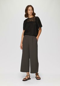 Zwarte top van gestructureerde stof met kantdetails, gecombineerd met een wijde donkere grijze broek en zwarte sandalen met bandjes. Minimalistisch ontwerp.